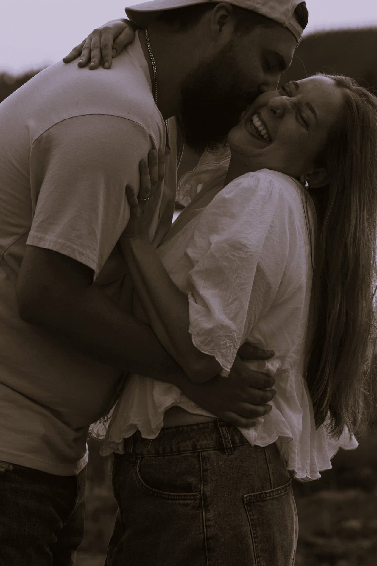 A black and white photograph of a couple embracing in tall grass