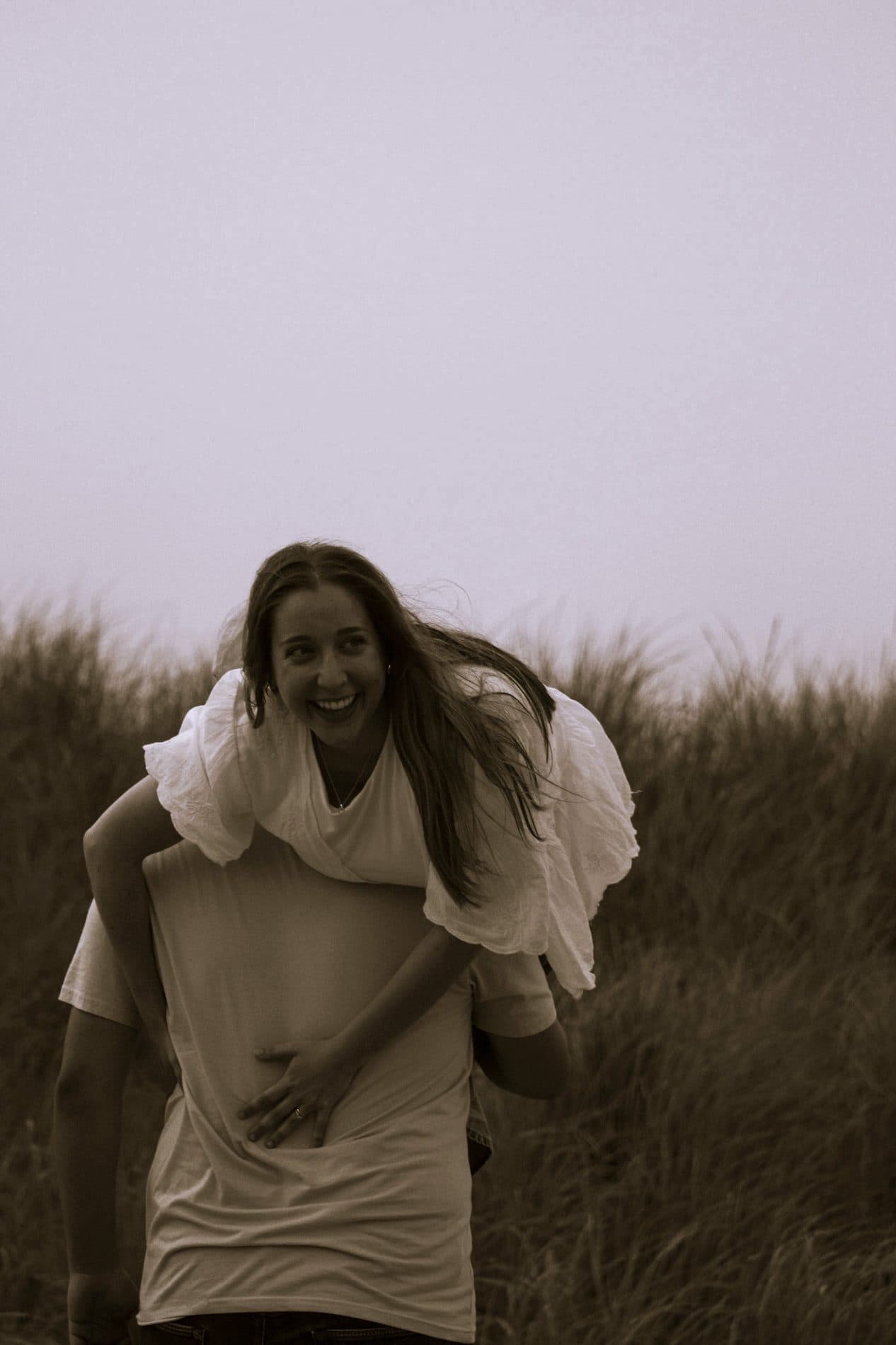 A black and white photograph of a woman laughing in a windswept field