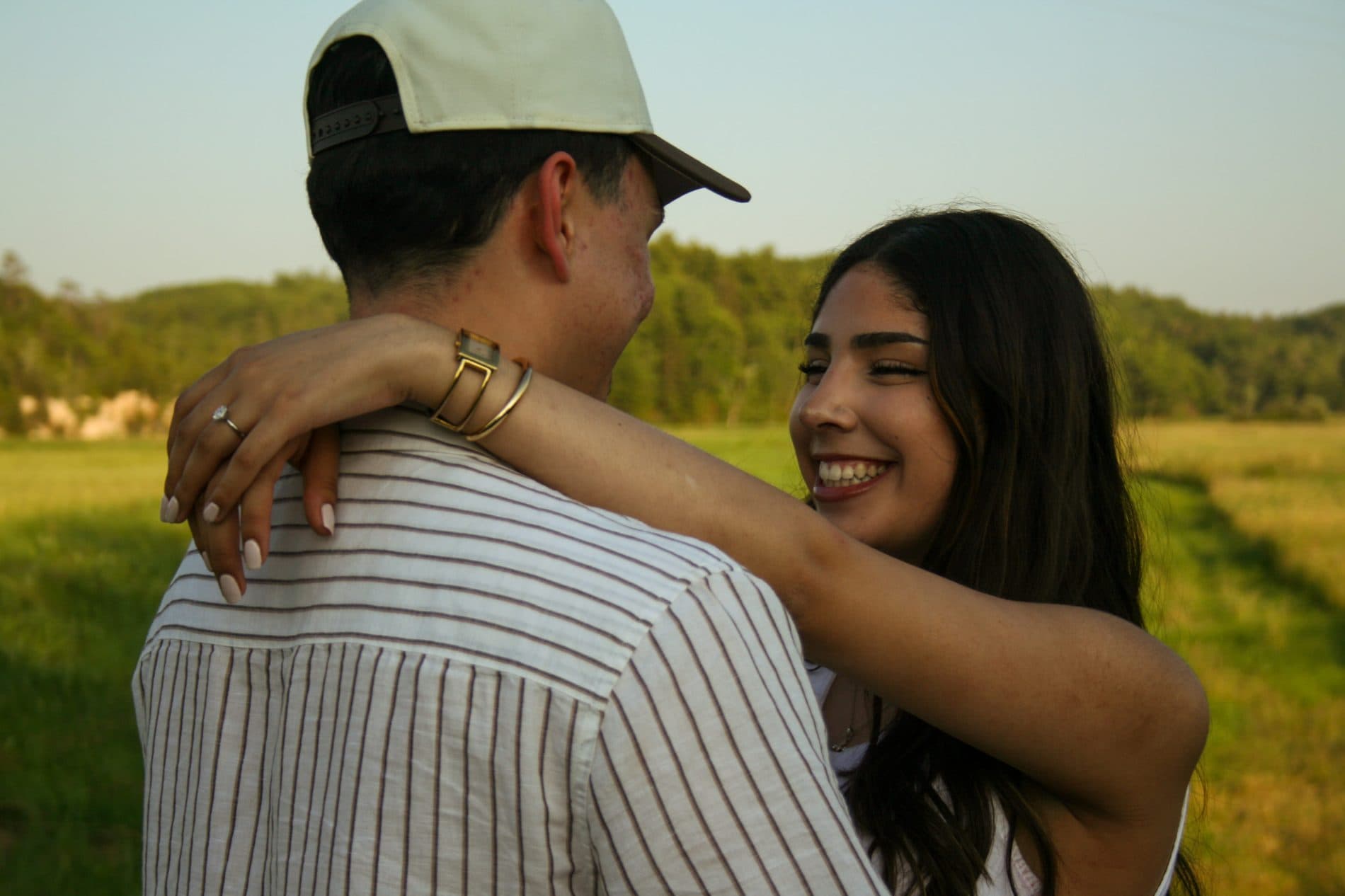 A couple embracing in an open field with rolling hills behind them