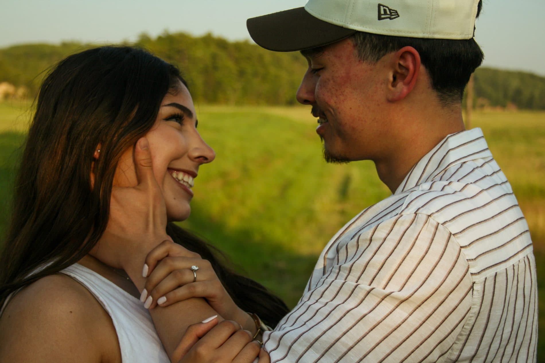 A couple standing close together in a green field at golden hour, looking at each other