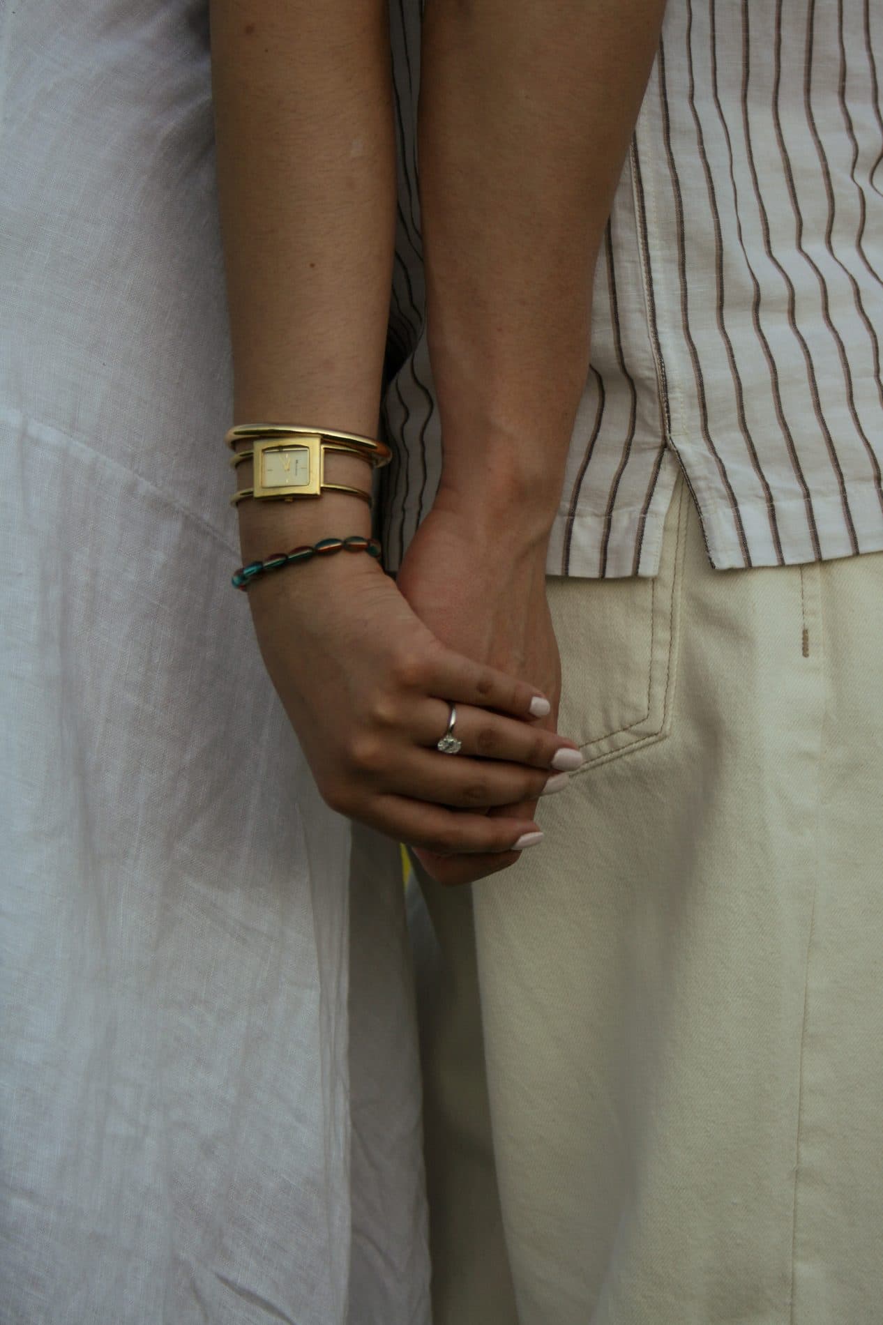 A quiet detail of clasped hands and a gold cuff bracelet