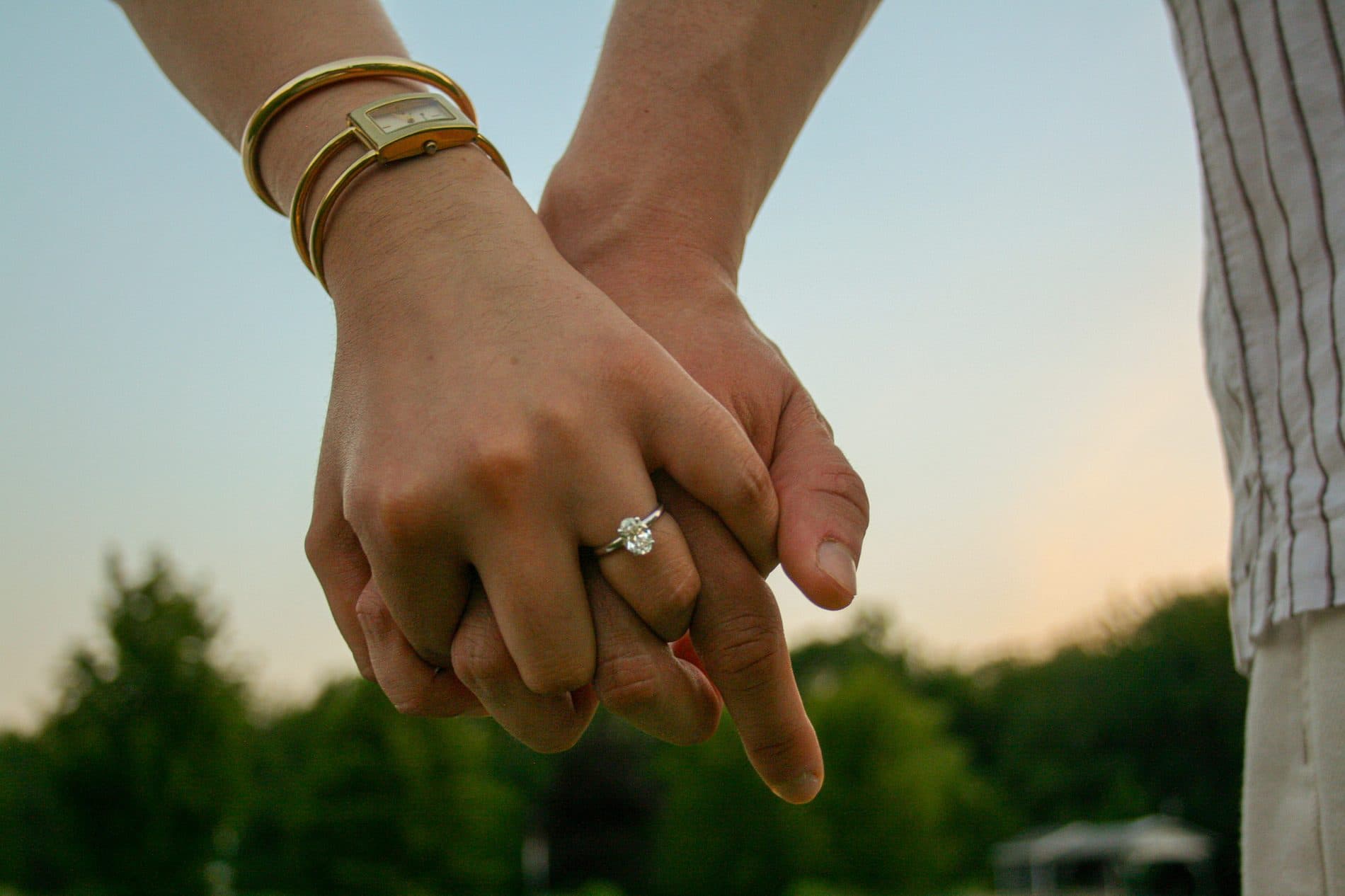 A close detail of linked hands with an engagement ring and gold bracelets