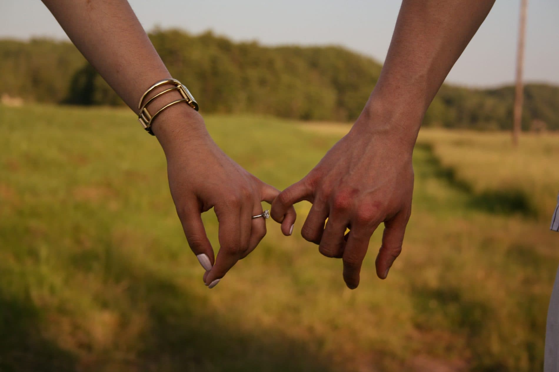 Two hands linked together, an engagement ring catching the light