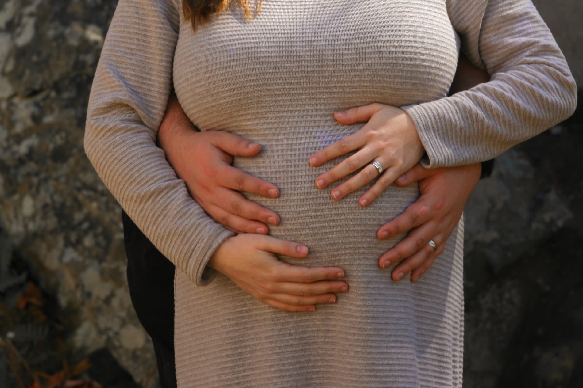 An expecting couple resting their hands together on the baby bump
